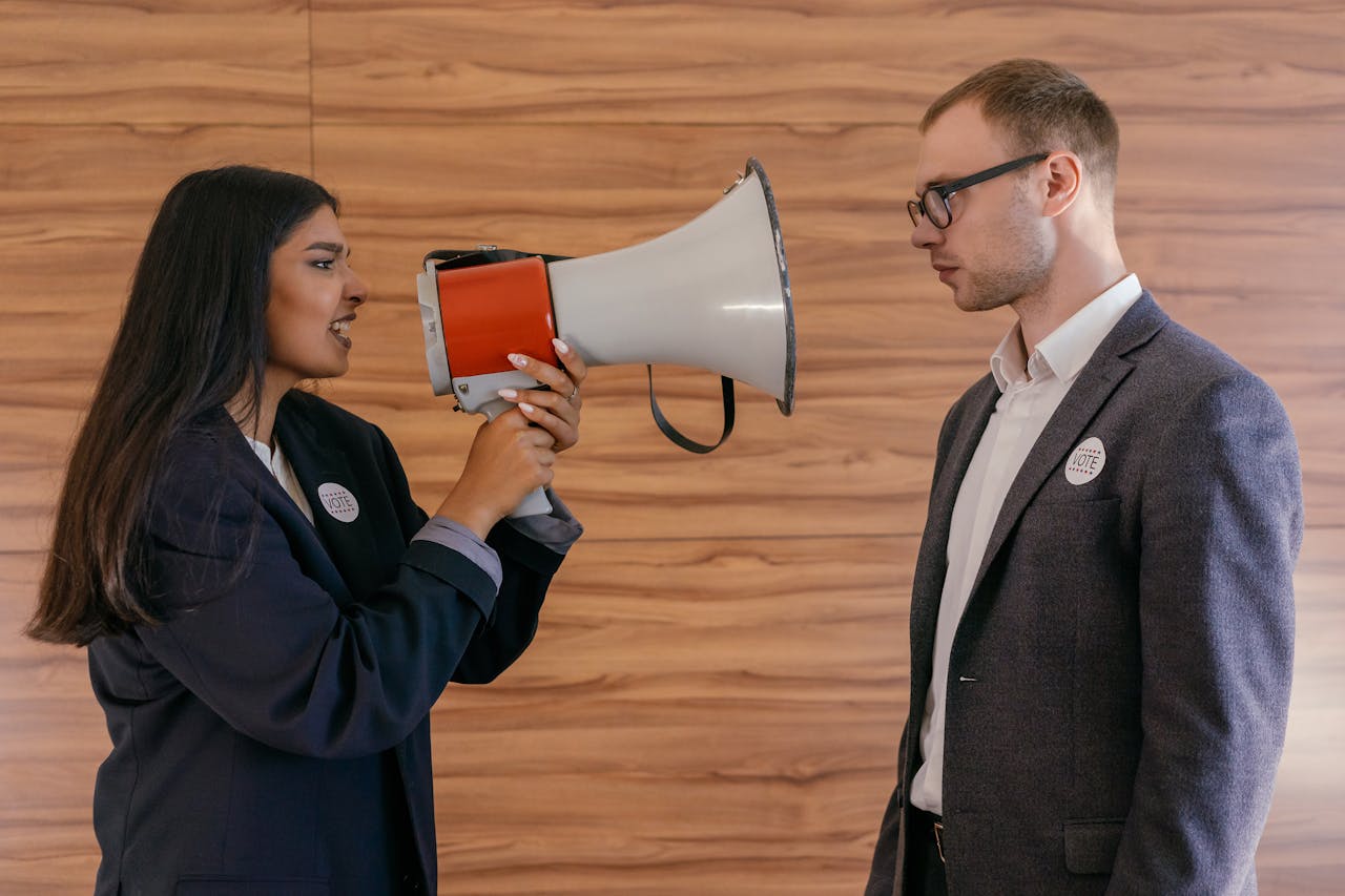 home-img A woman using a megaphone to confront a man in a suit indoors, symbolizing political debate.