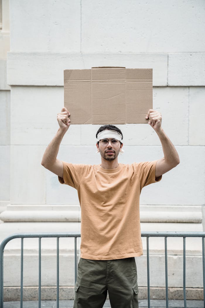 gallery-02 A man holds a blank cardboard sign during an outdoor protest by a building facade.